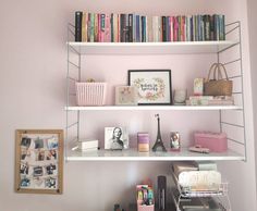 three white shelves filled with books and other items next to a framed photograph on the wall