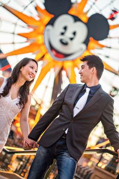 a man and woman holding hands in front of a ferris wheel