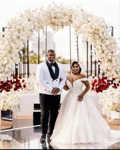 a bride and groom standing in front of a floral arch