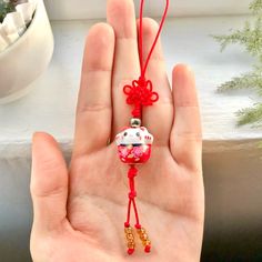 a hand holding a red string with a white cat on it