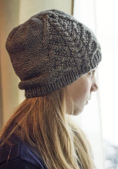 a woman standing next to a window wearing a knitted hat