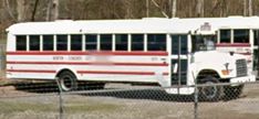 an old school bus is parked behind a chain link fence in front of some trees