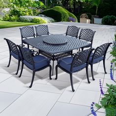 an outdoor table and chairs with blue cushions on a white tiled patio area surrounded by greenery