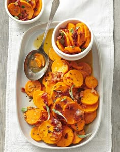 a white plate topped with sliced up sweet potatoes next to two bowls filled with sauce