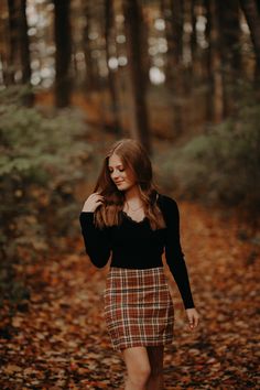 a young woman is walking through the woods in her plaid skirt and black sweater with brown boots