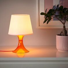 a table lamp sitting on top of a white counter next to a potted plant