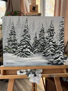 an easel with a painting on it that has snow covered trees in the background