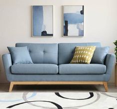 a living room with blue couches and two paintings on the wall above them,