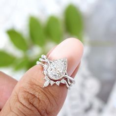 a close up of a person's hand holding a ring with a pear shaped diamond on it