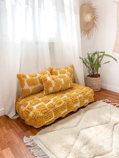 a yellow couch sitting in front of a window next to a white rug and potted plant