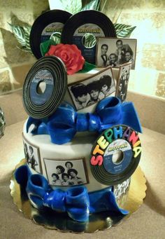 a three tiered cake decorated with pictures and blue ribbon, surrounded by cd's