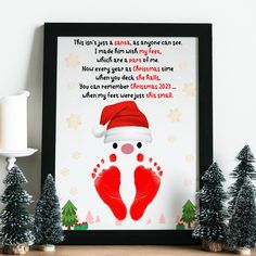 a framed christmas card with footprints and santa's hat on the shelf next to small trees