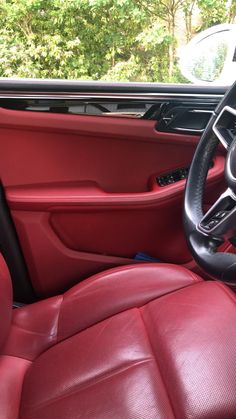 the interior of a car with red leather seats and steering wheel, trees in the background