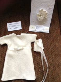 a baby's christ gown and card are on the couch next to an envelope