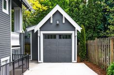 a gray garage with white trim on the front and side of it, next to a fence