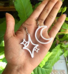 a hand holding two white earrings in it's palm, with the moon and stars on them