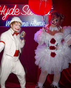 two people dressed in costumes standing next to each other holding balloons and posing for the camera