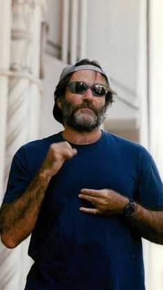 a man wearing sunglasses and a bandana standing in front of a building with his hand on his hip