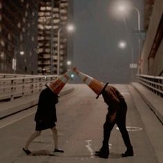 two people standing on the side of a road with traffic cones over their heads in front of them