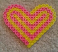 a pink and yellow heart made out of plastic beads on a carpeted floor with a gray background