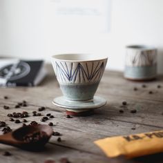 two cups sitting on top of a wooden table filled with coffee beans and chocolate chips