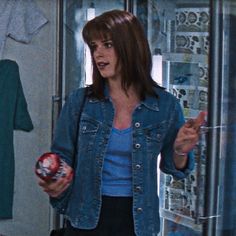 a woman in a blue shirt and jean jacket holding a red object while standing next to a glass door