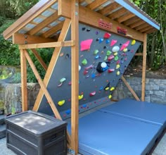 a rock climbing wall in the backyard with a blue mat under it and a black box