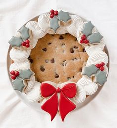 a christmas cookie decorated with holly leaves and red bows on a white platter, ready to be eaten