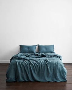 a bed with two pillows on top of it in front of a white wall and wooden floor