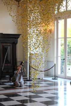 a woman taking a photo with her cell phone in the middle of a room filled with yellow flowers