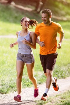 a man and woman running on a path in the park, one is wearing an orange shirt