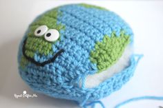 a crocheted blue and green object with eyes on it's face, sitting on a white surface