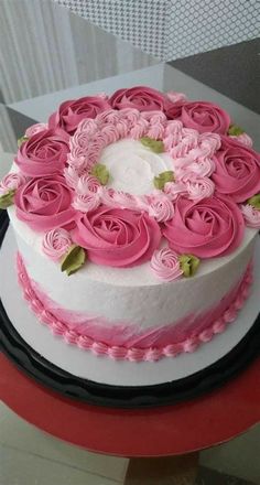 a white cake with pink frosting and flowers on top is sitting on a table