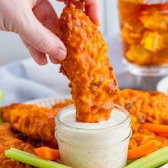 a person dipping something into a small jar filled with ranch chicken wings and celery sticks