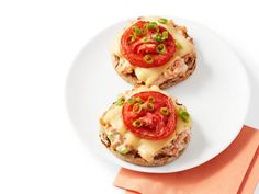 two open faced sandwiches with cheese and tomatoes on them sitting on a white plate next to an orange napkin