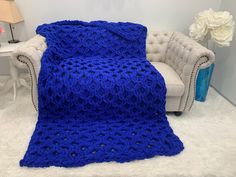 a blue crocheted blanket sitting on top of a white couch next to a chair