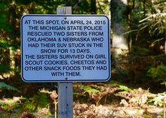 a white sign with black writing on it in front of some trees and dirt ground