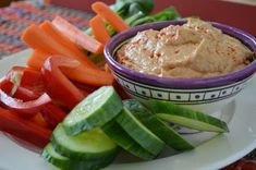 a white plate topped with cucumbers and carrots next to a bowl of hummus