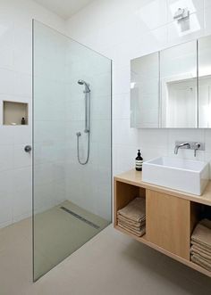 a bathroom with a walk in shower next to a white sink and wooden counter top