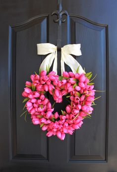 a heart shaped wreath with pink tulips hanging on a black front door,