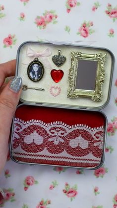 someone is holding an open tin box with various items in it on a floral tablecloth