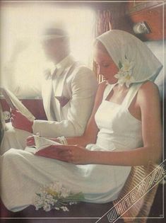 a man and woman dressed in white sitting next to each other on a couch reading