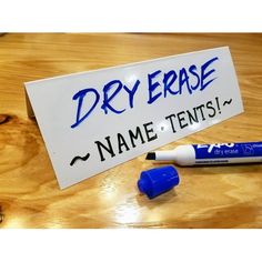 a dry erase marker next to two markers on a table with a name tag attached