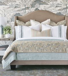 a bed with pillows and blankets on top of it in front of a wallpapered background