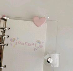 an open journal with a pink heart on the cover next to a toilet paper dispenser