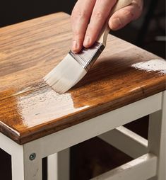 a person using a brush to paint a wooden table with white paint on top of it