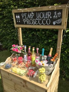 a wooden stand with various drinks and condiments on it in front of some bushes