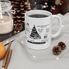 a white coffee mug sitting on top of a table next to an orange and some pine cones