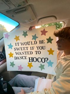 a person sitting in a car holding a sign that says, it would be sweet if you wanted to dance hoco?