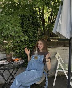 a woman in overalls sitting on a chair with her hand up to the side